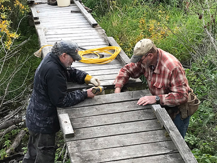 Two volunteers stand in the wetlands as they repair a boardwalk at Scout Island Nature Centre.